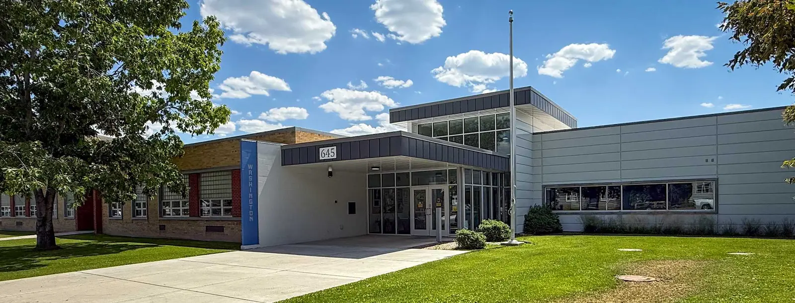 A view of a modern school building exterior with a lawn and blue sky.