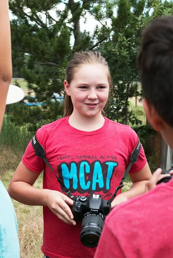 A girl with a camera in front of a group of people.