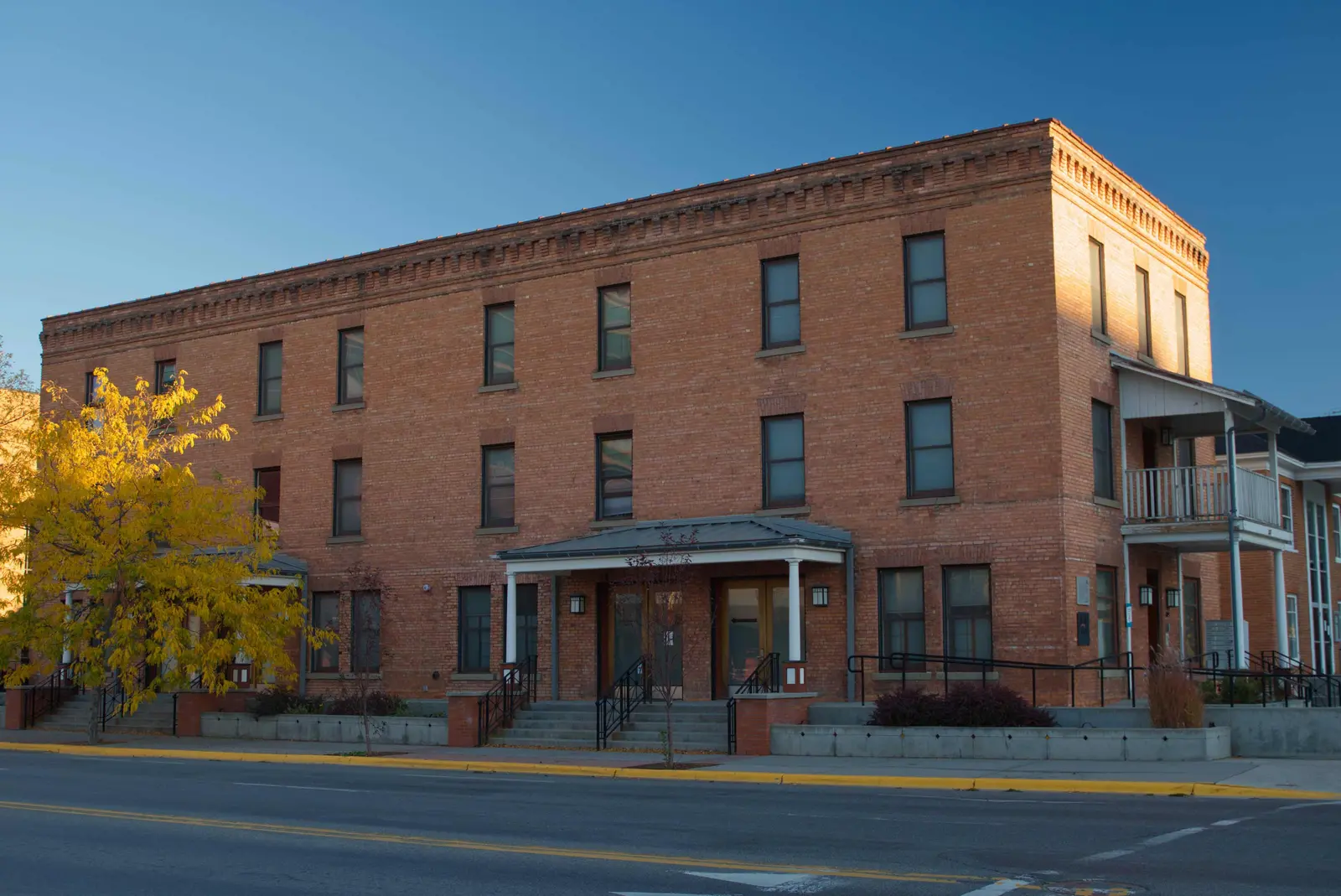 A three-story brick building sits along a street under a clear blue sky.