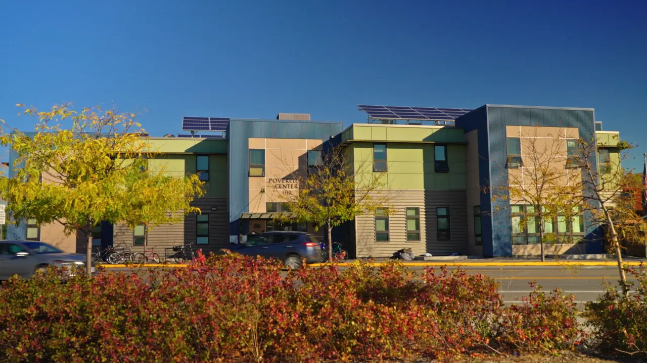 A colorful modern building with solar panels on the roof sits behind autumn trees and a road.