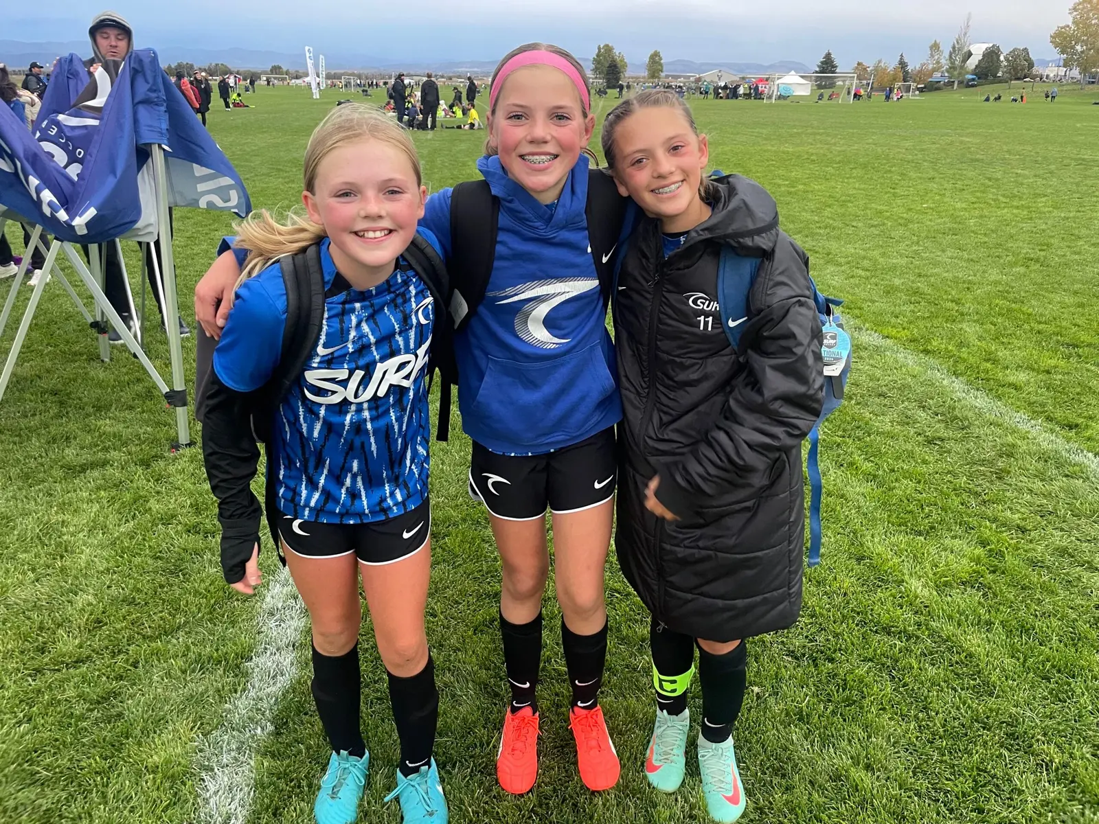 Three young soccer players stand together on a grassy field.