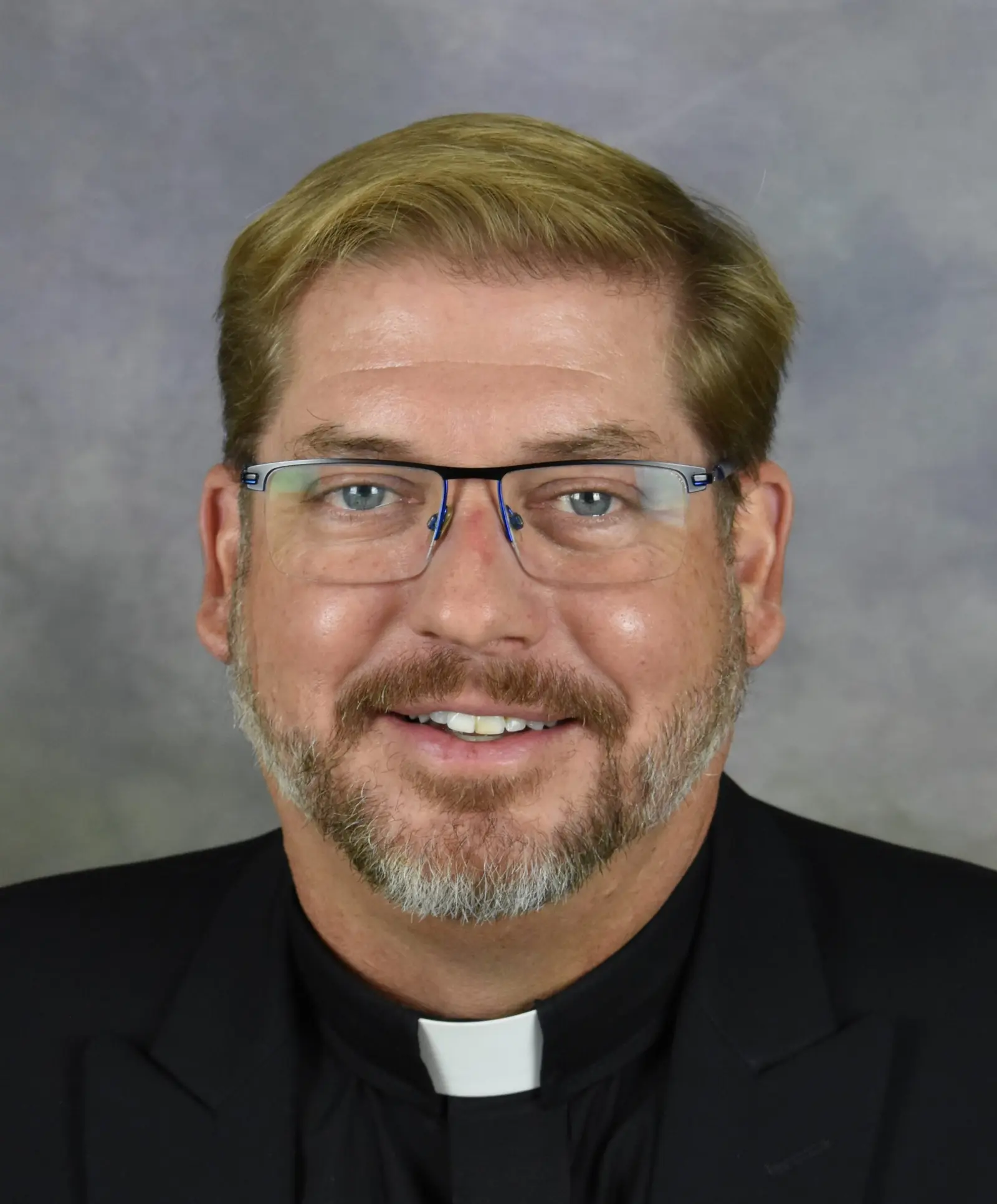 A portrait of a man wearing glasses and a clerical collar.