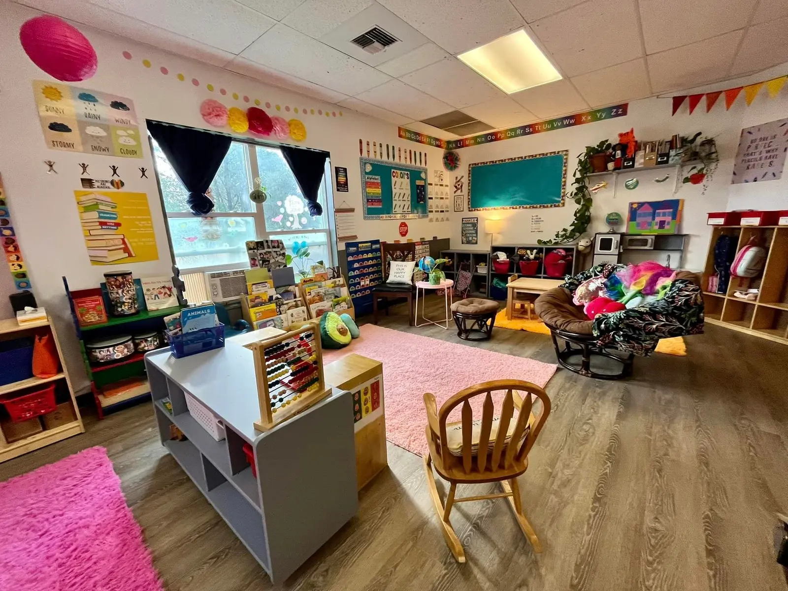 A brightly decorated, colorful classroom is filled with child-sized furniture, books, and learning materials.
