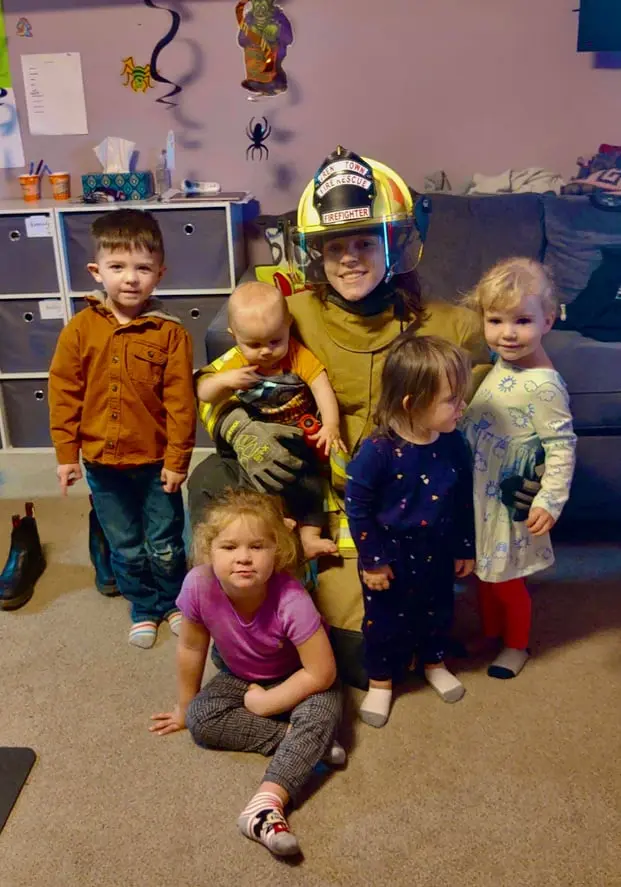 A firefighter in uniform poses for a photo while surrounded by several children.
