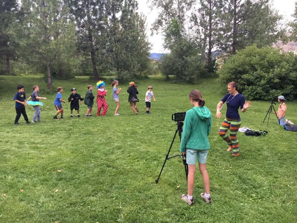 An adult leader and a group of children participate in an outdoor activity in a park.