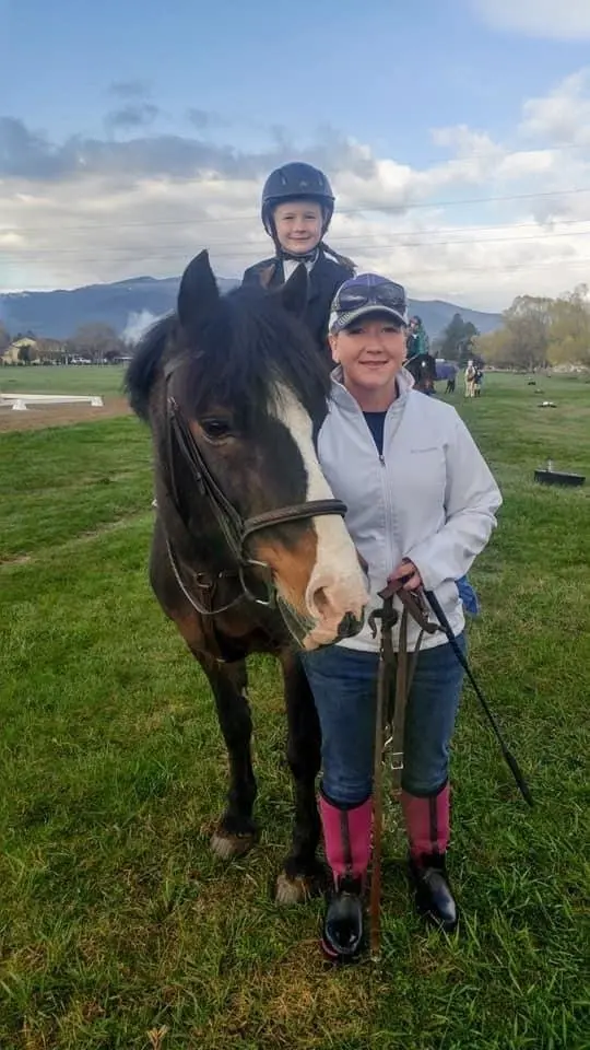 A woman leads a horse with a child riding on its back in an outdoor field.
