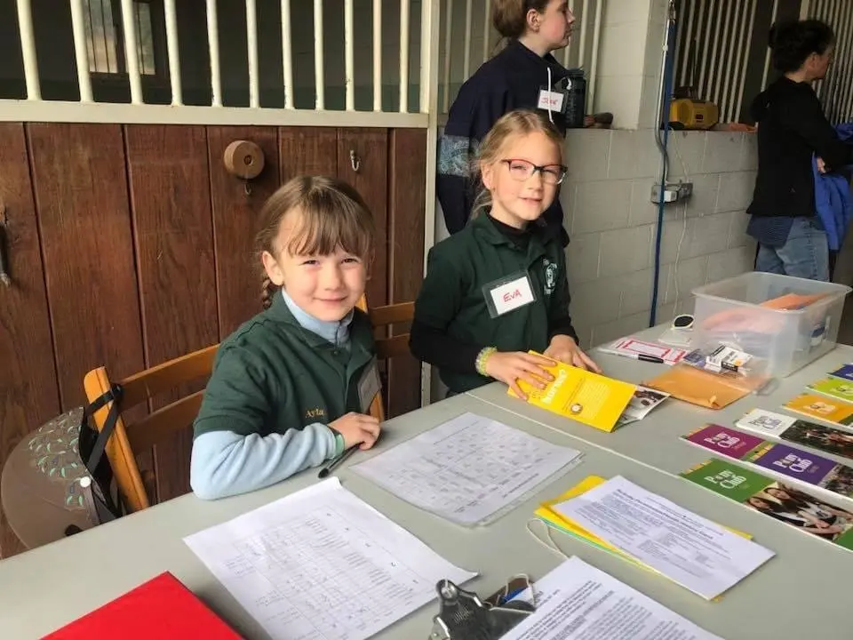 Two girls wearing name tags sit at a table with papers and informational materials.