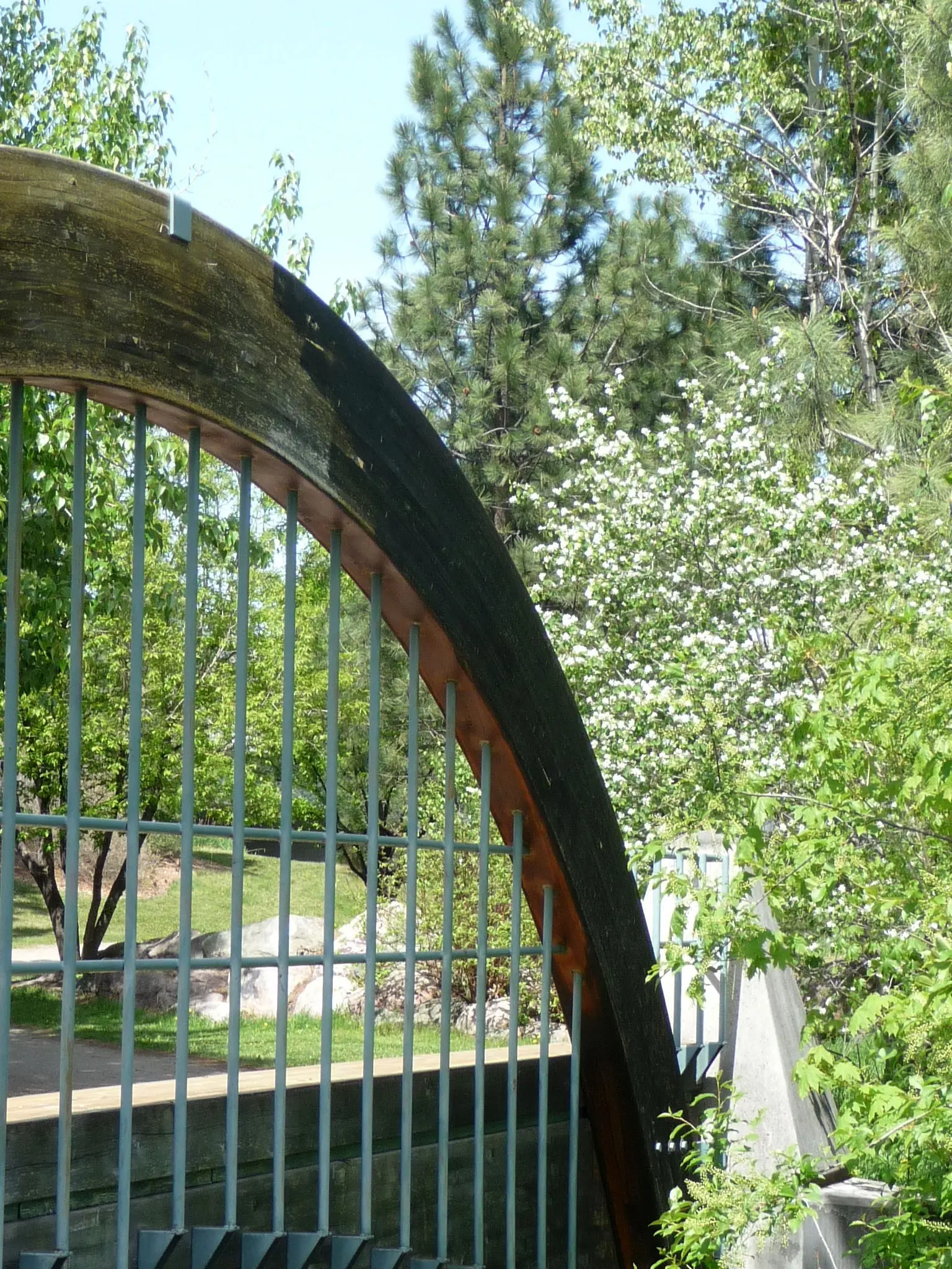 A decorative arched wooden and metal structure stands in a lush garden setting.
