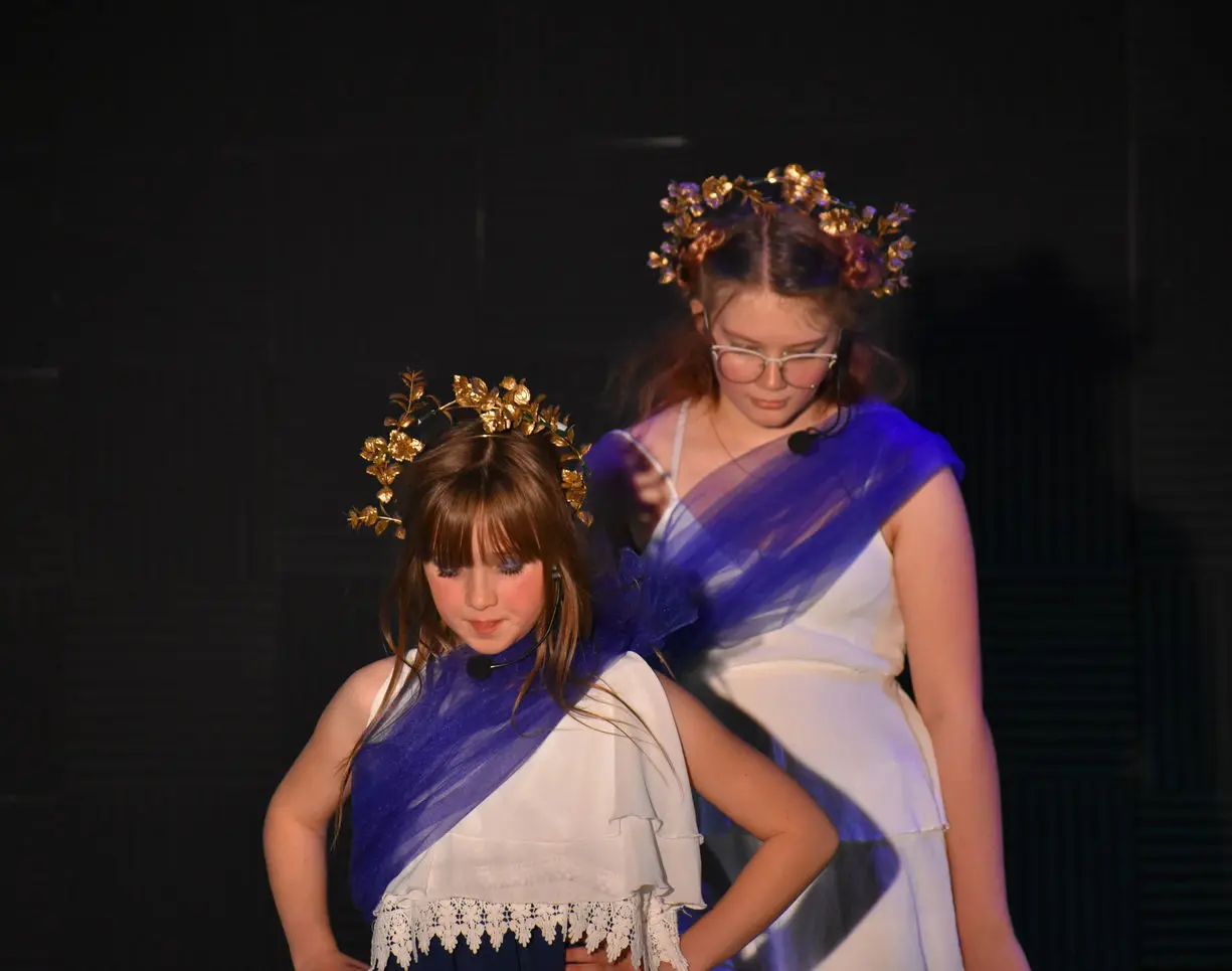 Two girls in costumes with headpieces perform on stage.
