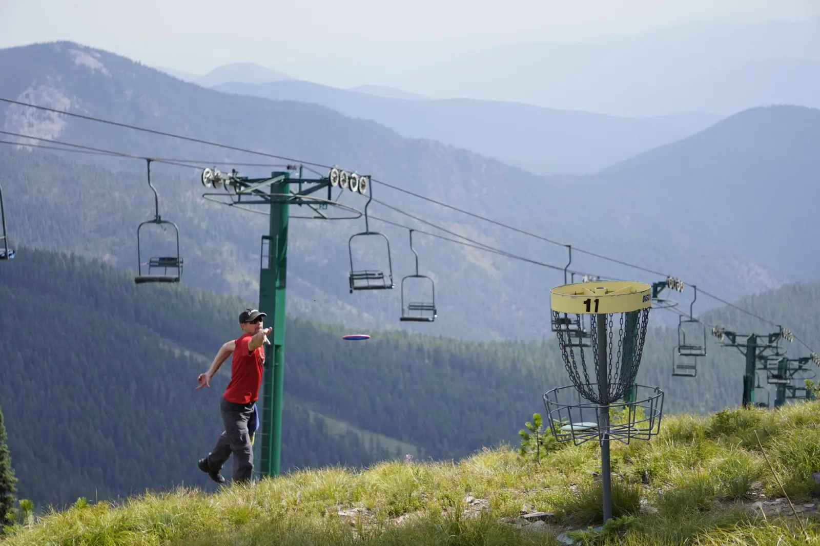 A man plays disc golf on a mountain slope with ski lifts in the background.