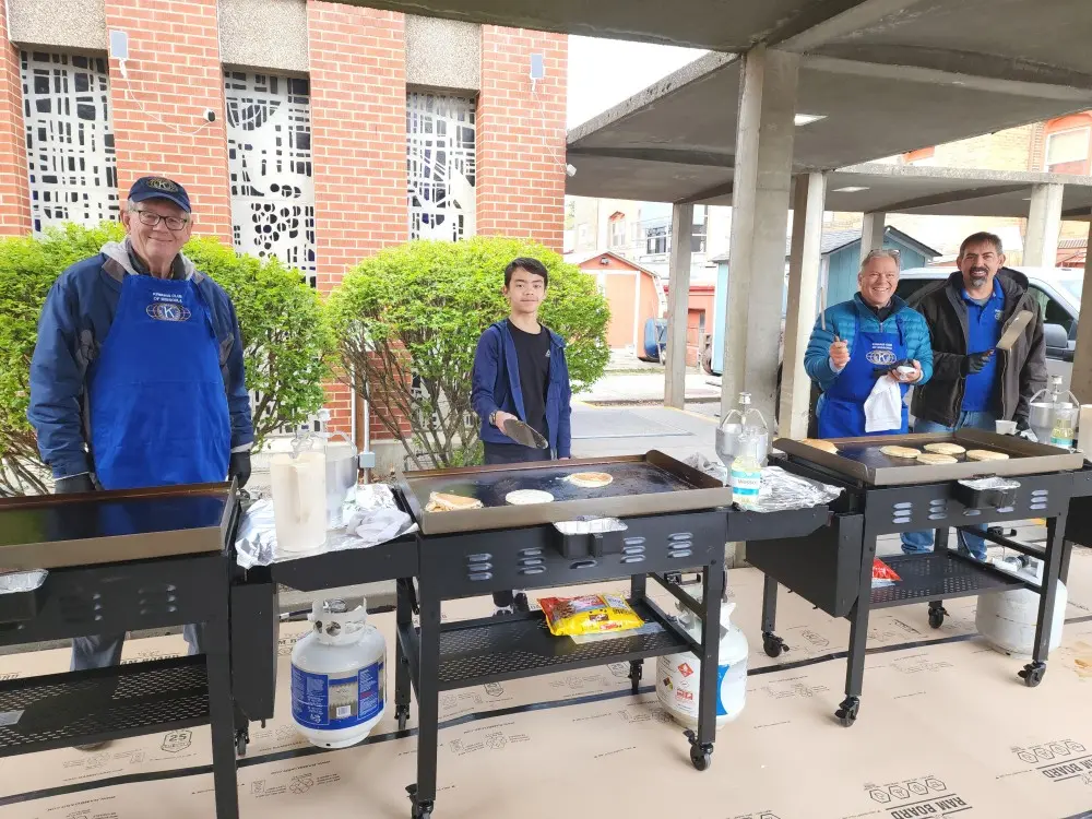 Three men and a young person are cooking pancakes on outdoor grills.