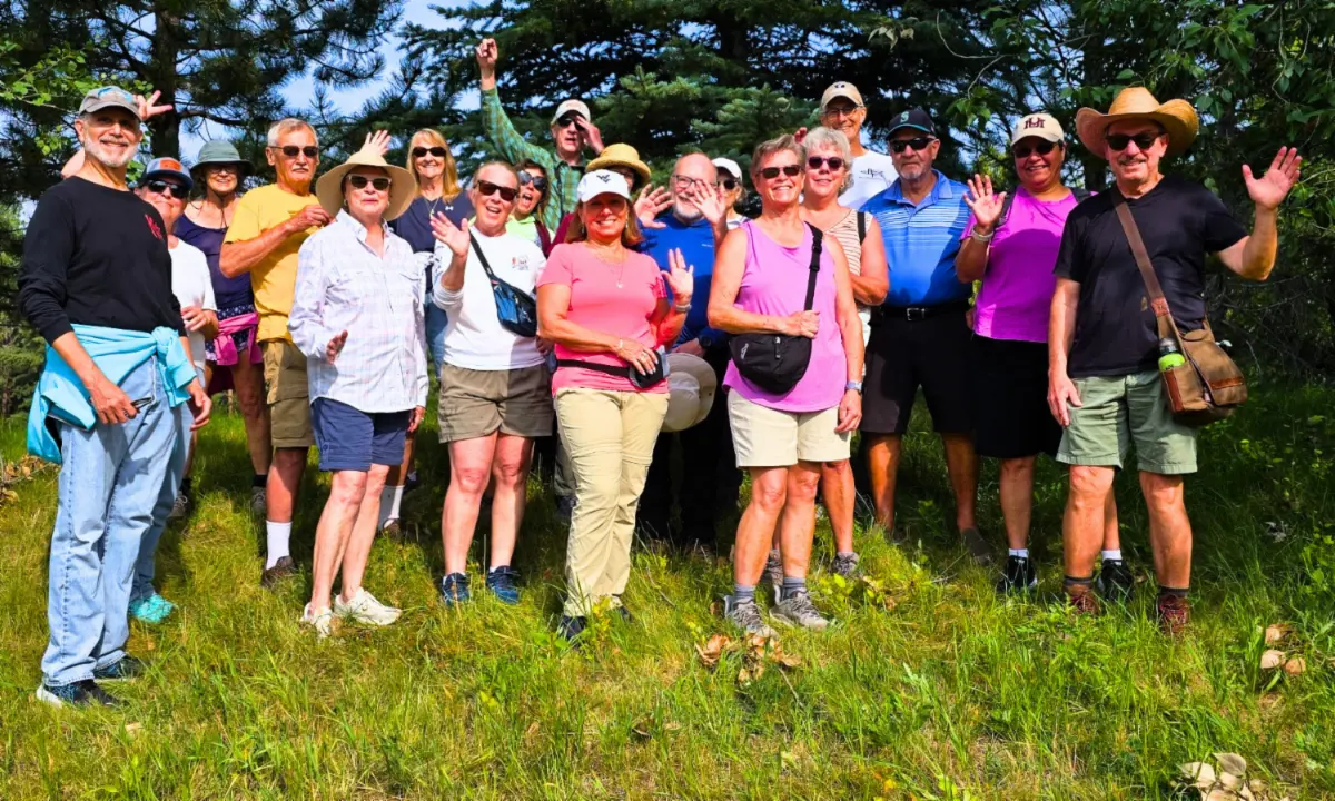 A large group of adults standing outdoors in a grassy area with trees behind them.