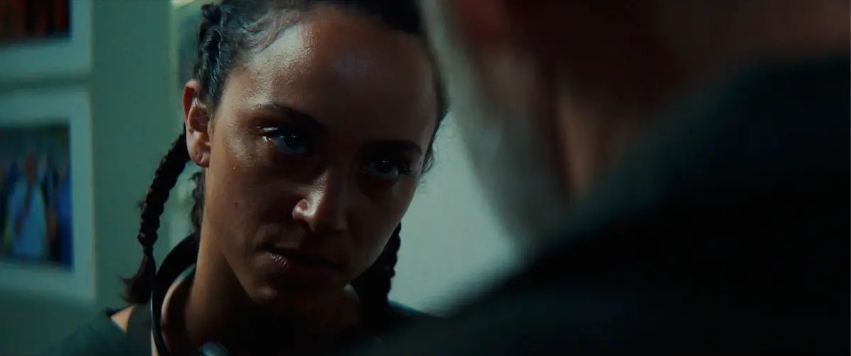A woman with braided hair looks intently at an individual whose back is turned toward the camera.