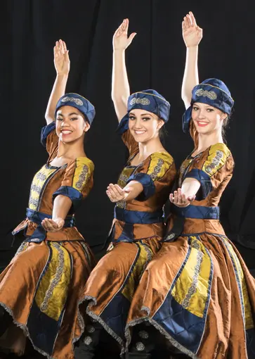 Three young women in traditional-style folk costumes perform a choreographed dance pose.