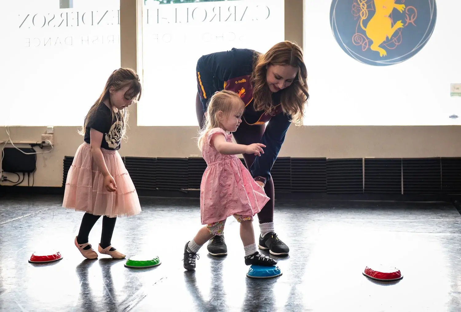 An instructor helps young children practice dancing with colorful steps in a studio.