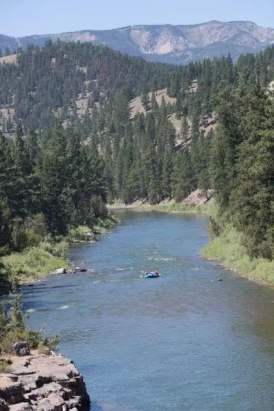 Photo from montanastateparks.reserveamerica.com A small raft floats down a river surrounded by forested mountains.
