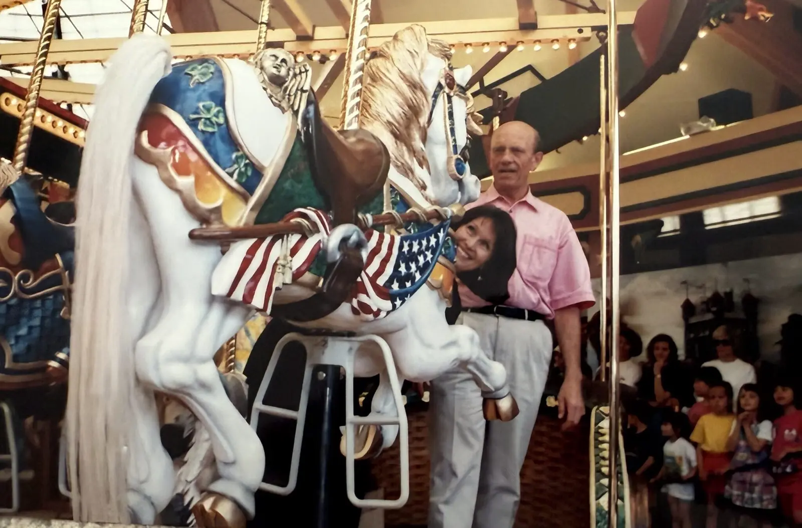 A man and a woman pose next to a carousel horse while others stand nearby in the background.