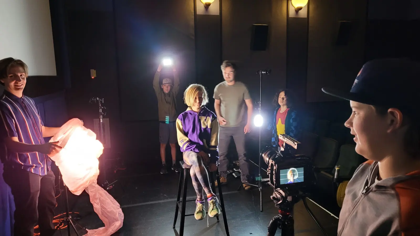 A group of young people and an adult collaborate to film a video in a studio setting.