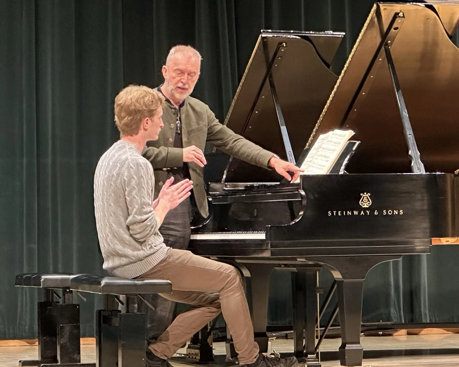 An instructor guides a student at a grand piano.
