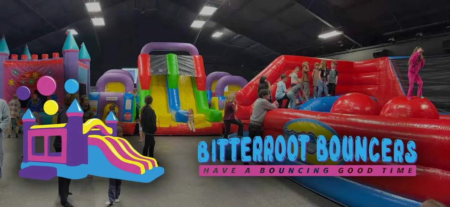 Children play on large inflatable bounce houses and slides in an indoor facility.