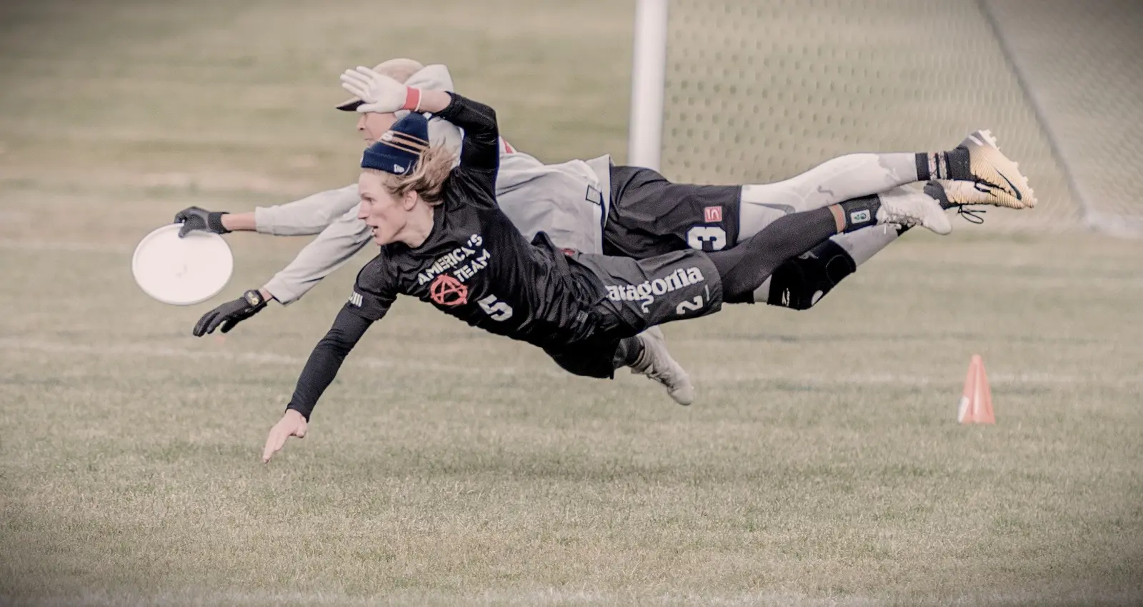 A frisbee player dives horizontally across a field during a game.