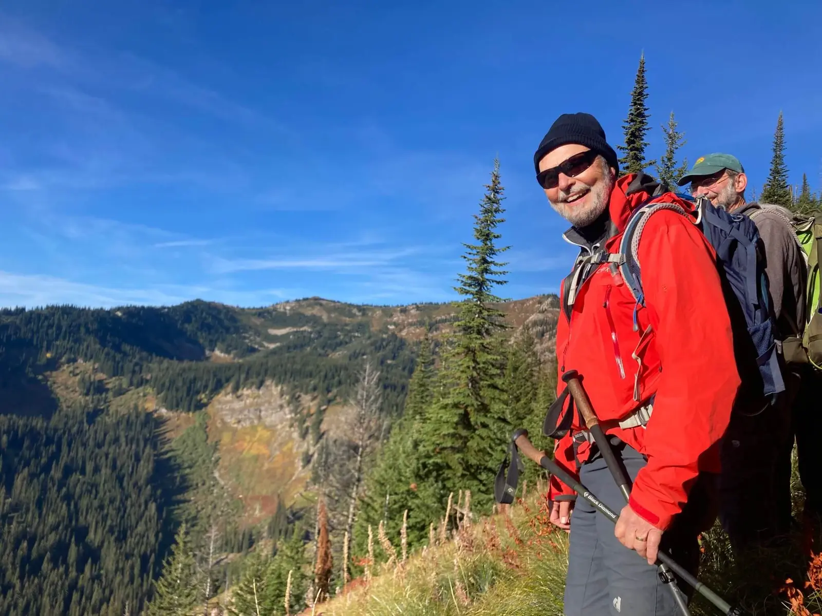 Two men hike along a mountain trail on a sunny day.