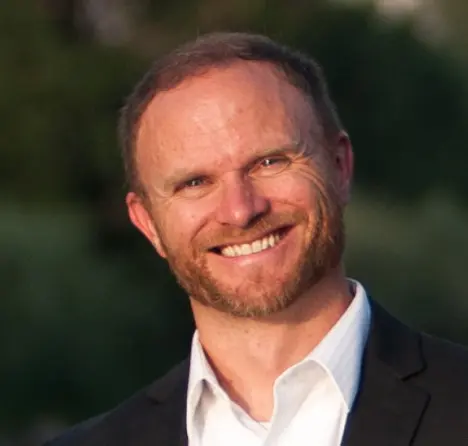 A headshot of a smiling man wearing a white shirt and a dark suit jacket.