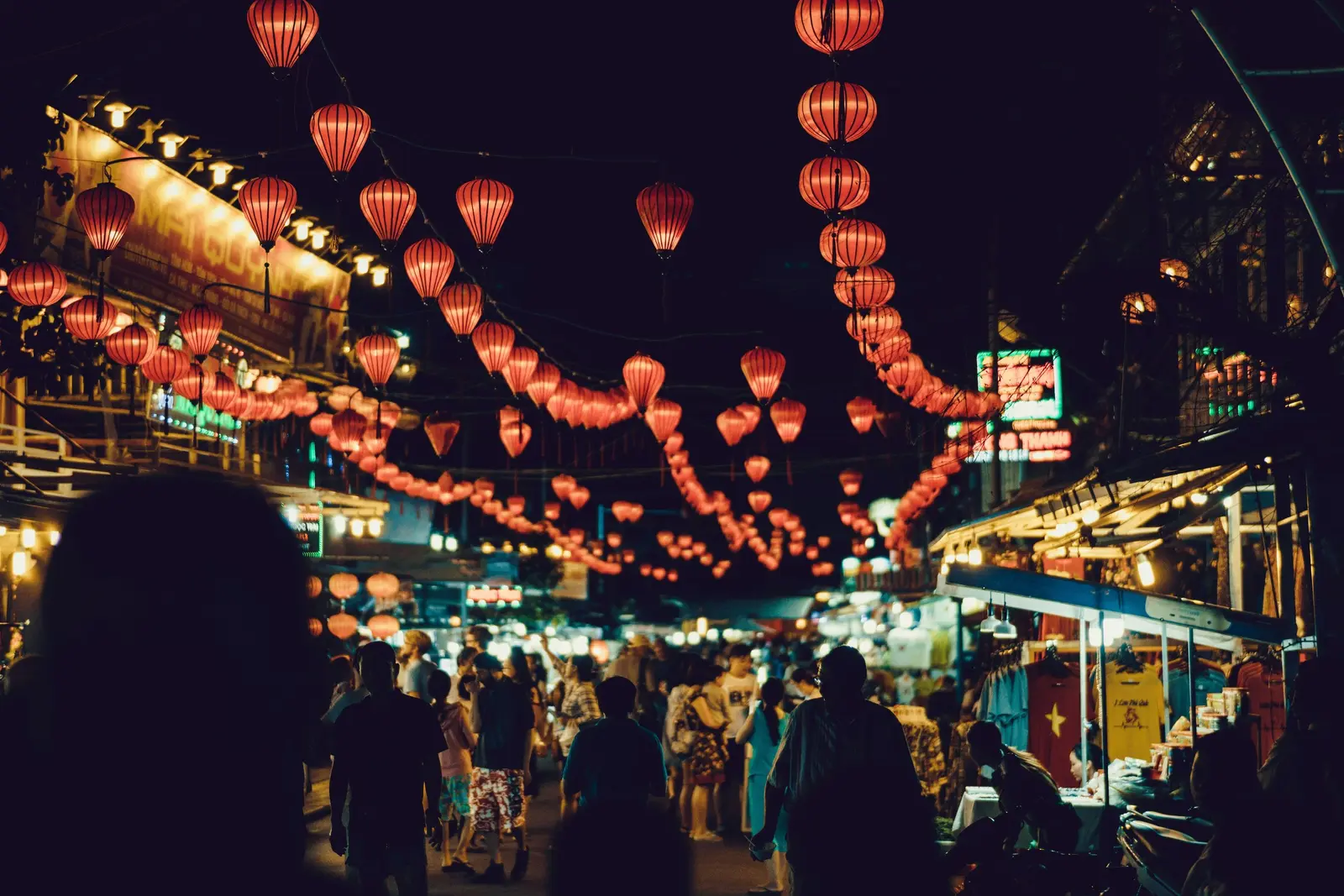A busy night market is illuminated by rows of hanging red lanterns.