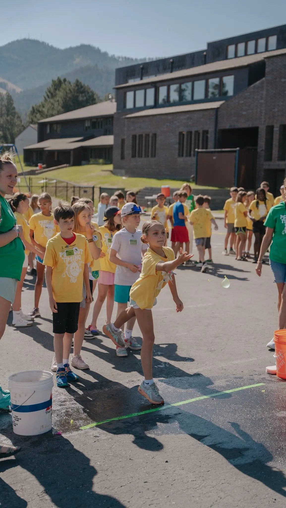 A group of children in yellow shirts participate in a water balloon toss game outdoors on a sunny day.