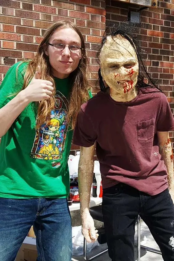 Two people posing for a photo. The person on the right is wearing a zombie mask.