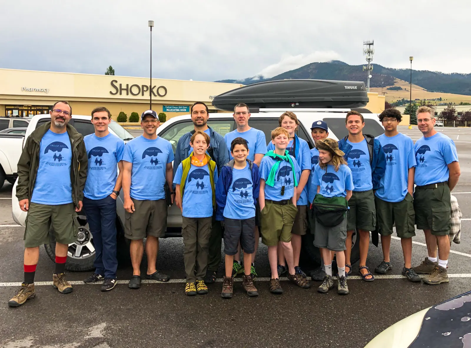A large group of children and adults in matching blue t-shirts pose together in a parking lot.