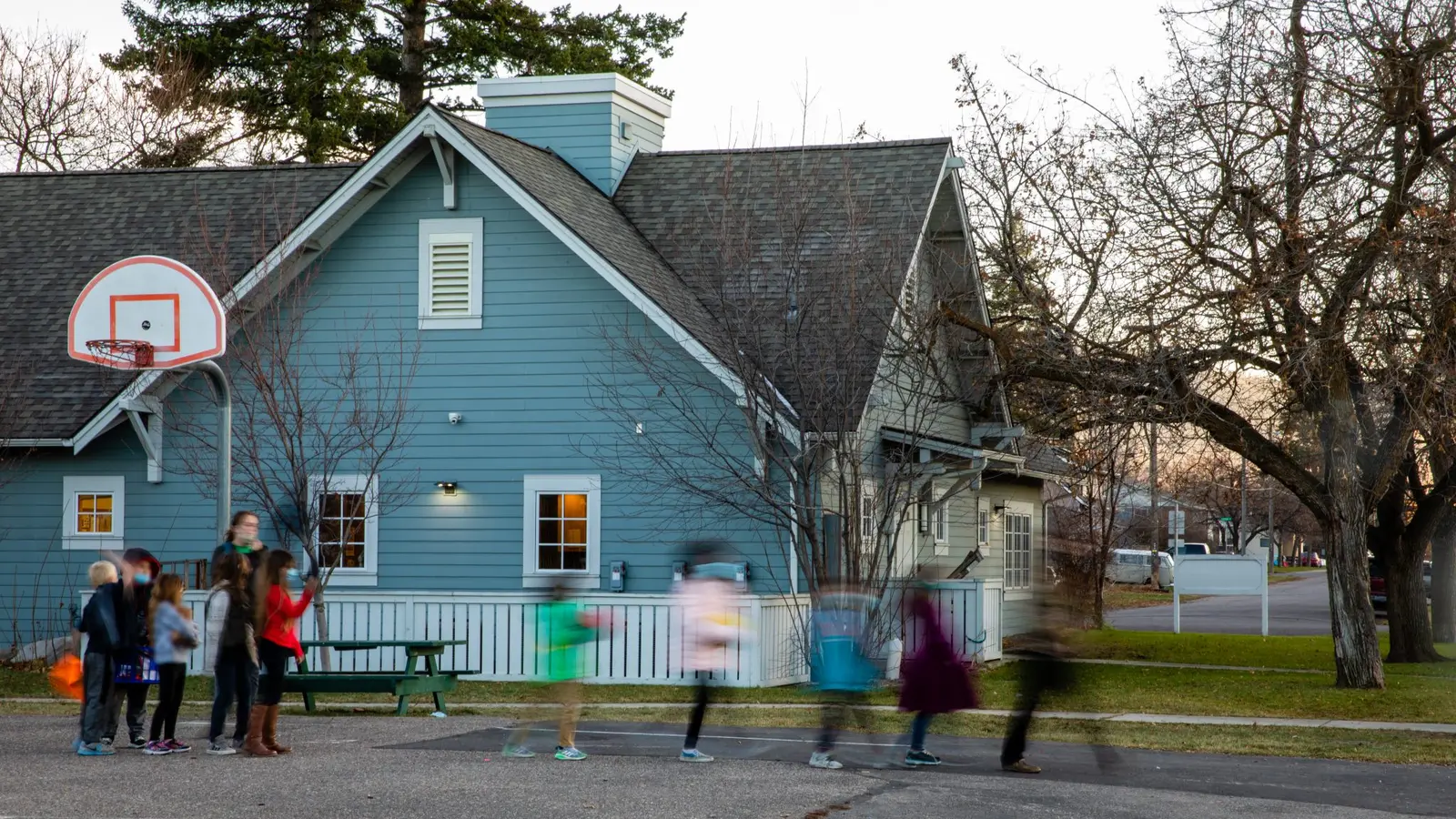 A group of children are gathered in front of a blue building with a basketball hoop.