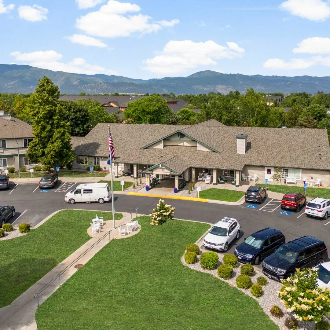 An aerial view shows a building with a large parking lot and mountain landscape in the background.