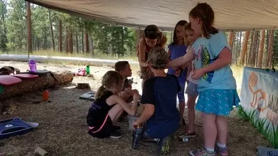 A group of children and an instructor participate in an outdoor educational activity under a canopy.