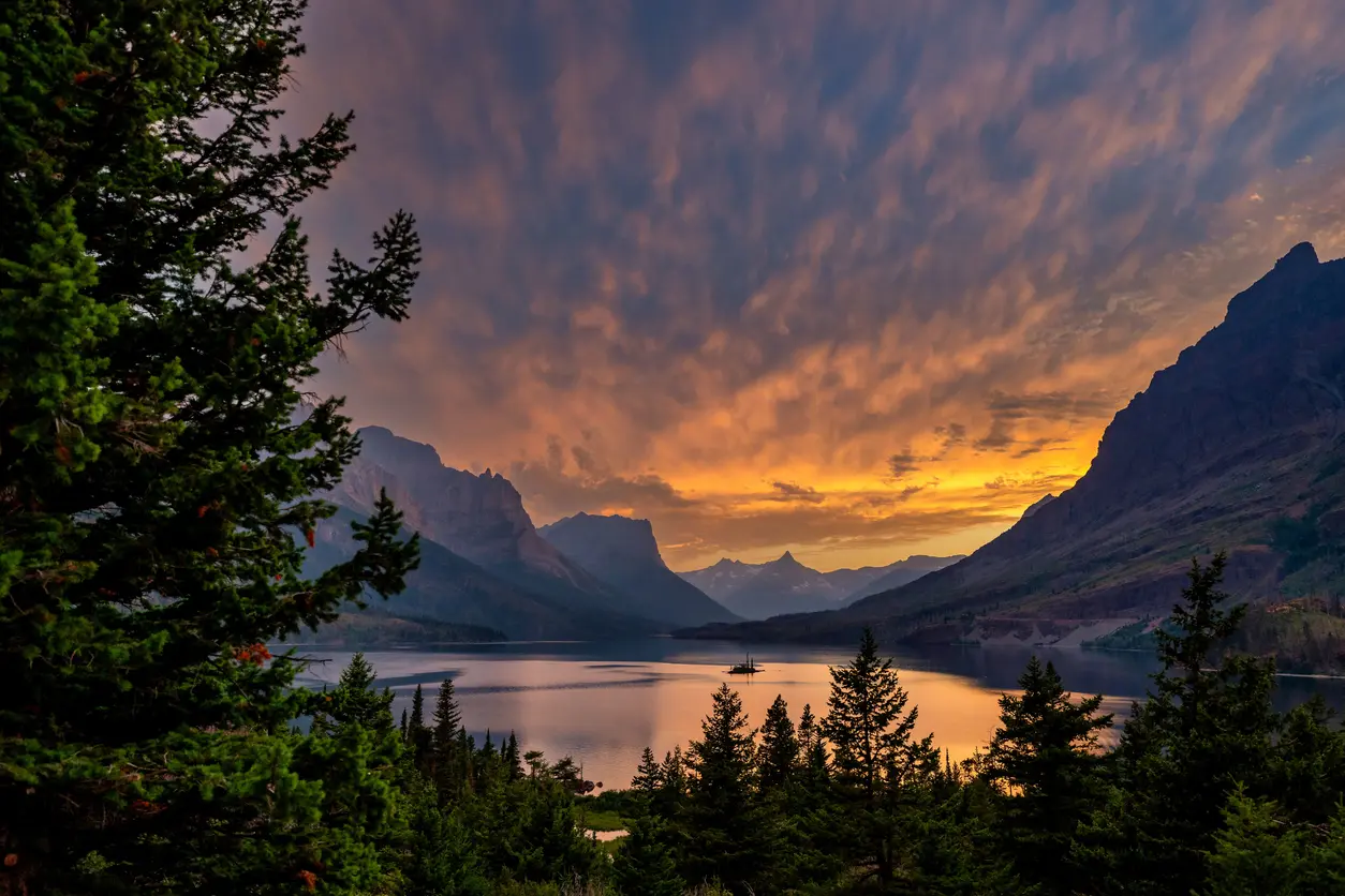 Sunset over a mountain lake with pine trees in the foreground.