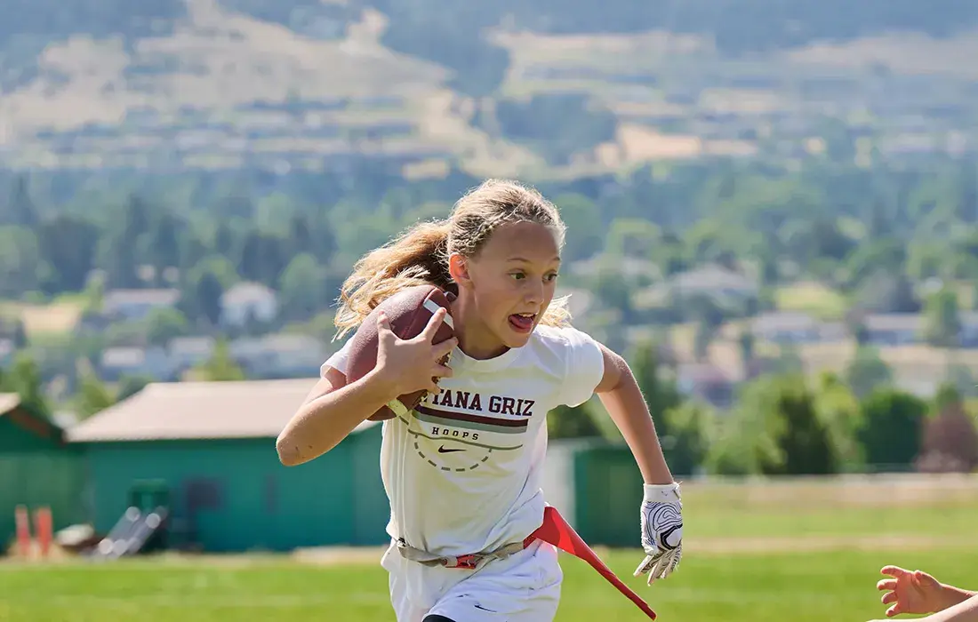 A young girl runs while holding a football during an active game.