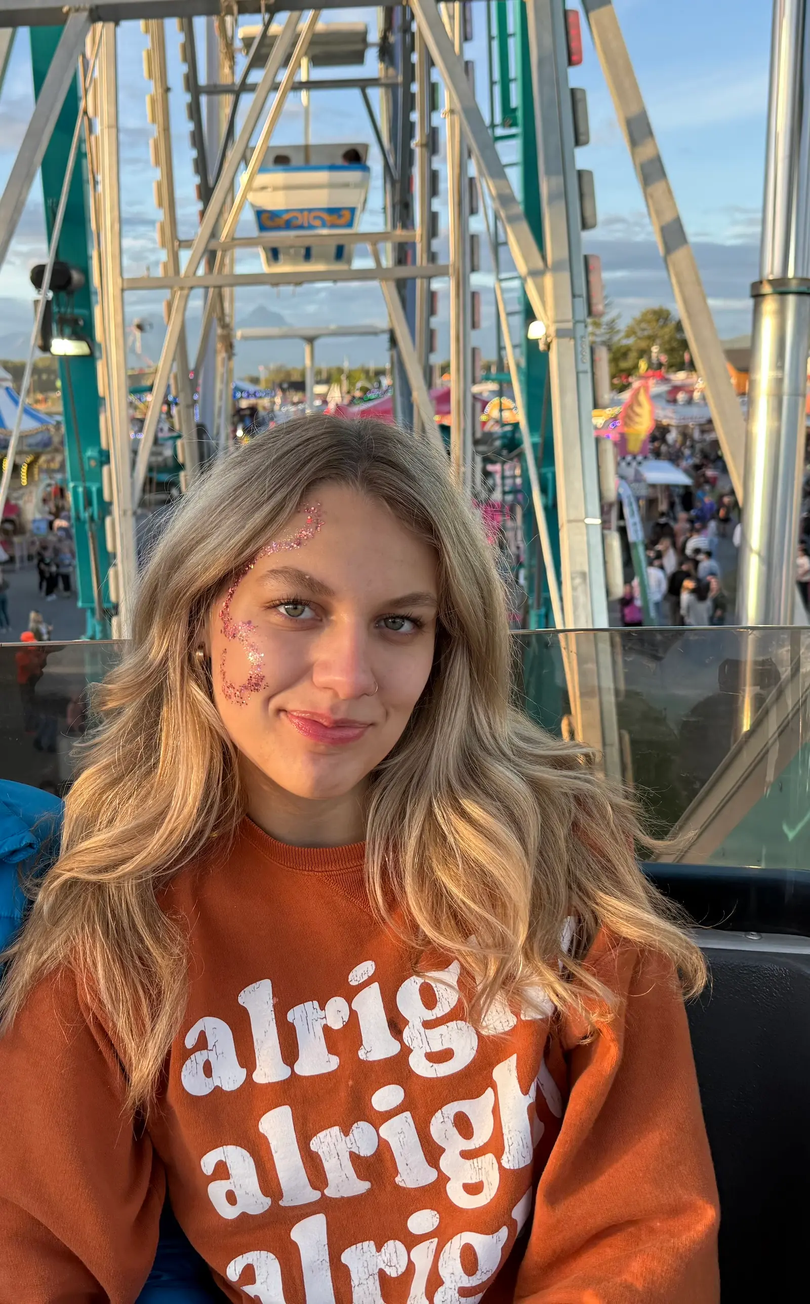 A young woman sits on a Ferris wheel at a carnival.