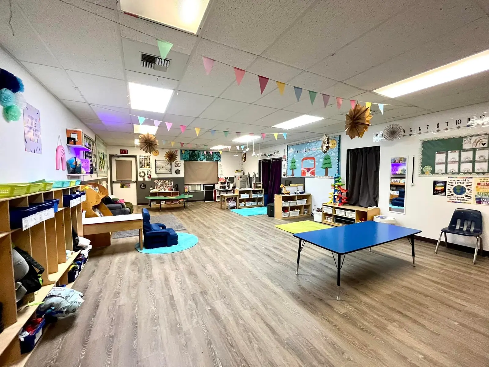 An empty, brightly decorated classroom for children features tables, storage shelves, and educational decorations.