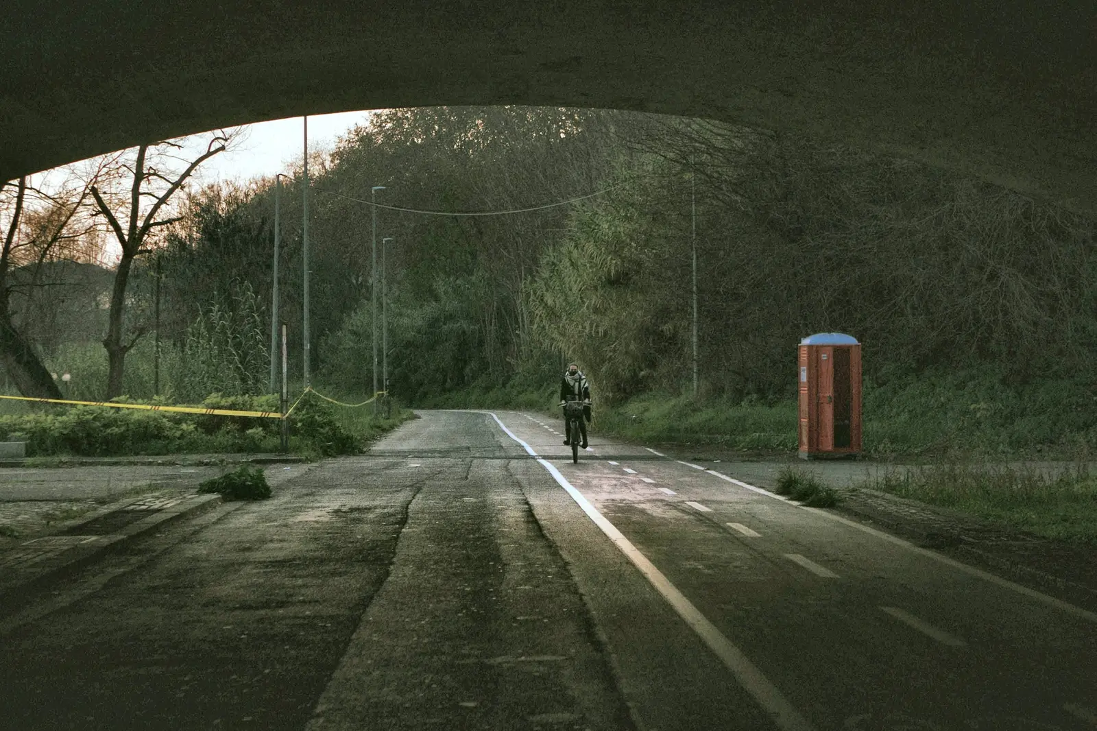 A person rides a bicycle along a path under a bridge in a wooded area.