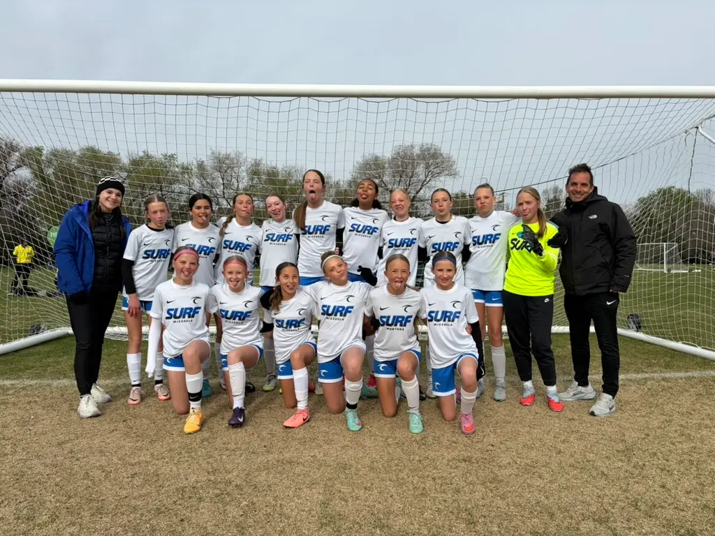 A youth soccer team poses for a group photo in front of a goal net.