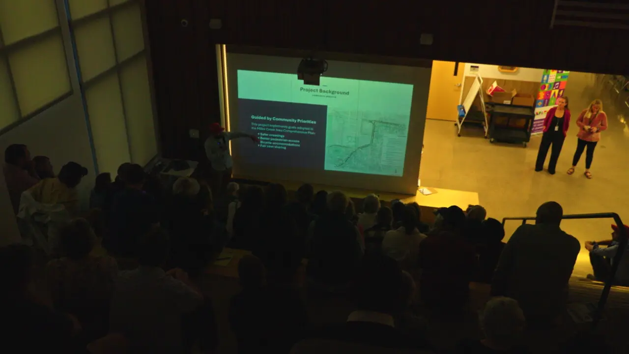 People sit in a dark room watching a presentation on a screen about community priorities.
