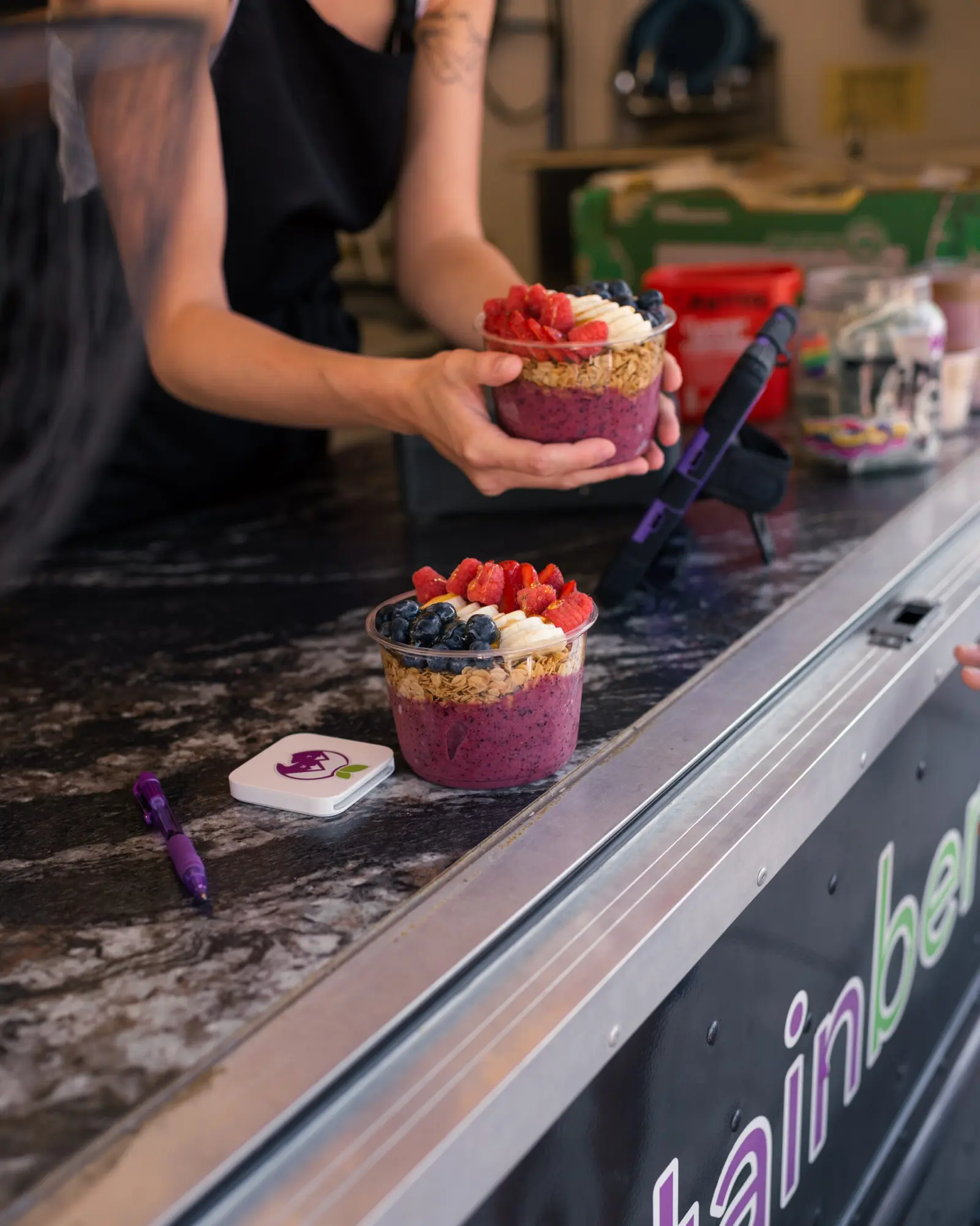 A person holds a fruit and granola smoothie bowl while another bowl sits on the counter in front of them.