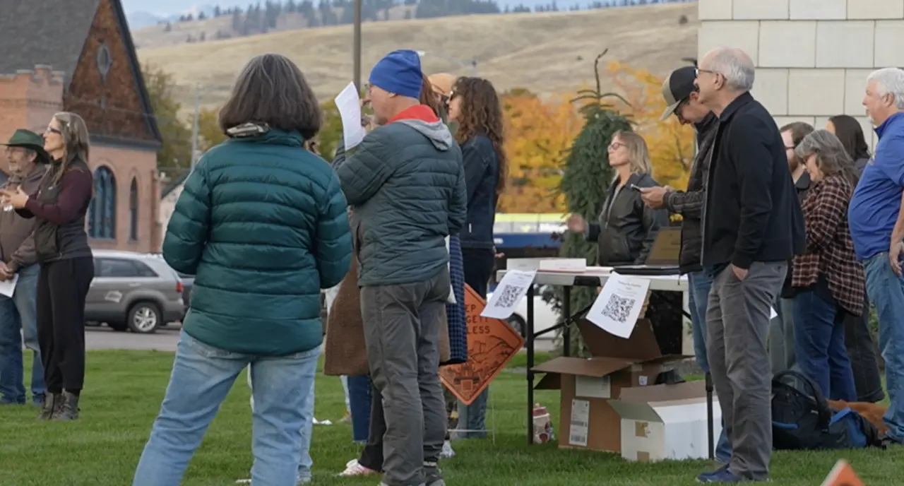 A group of adults gathers outdoors near a folding table with informational flyers.