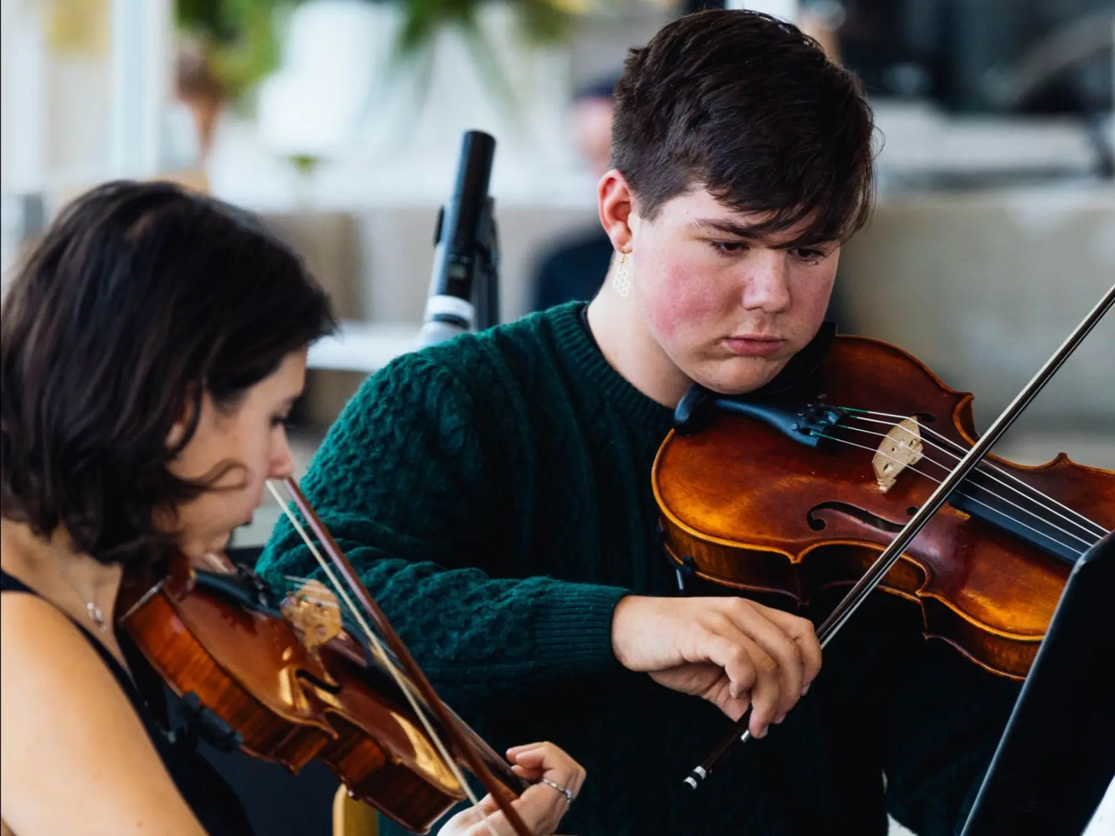 Two people play violins while performing.