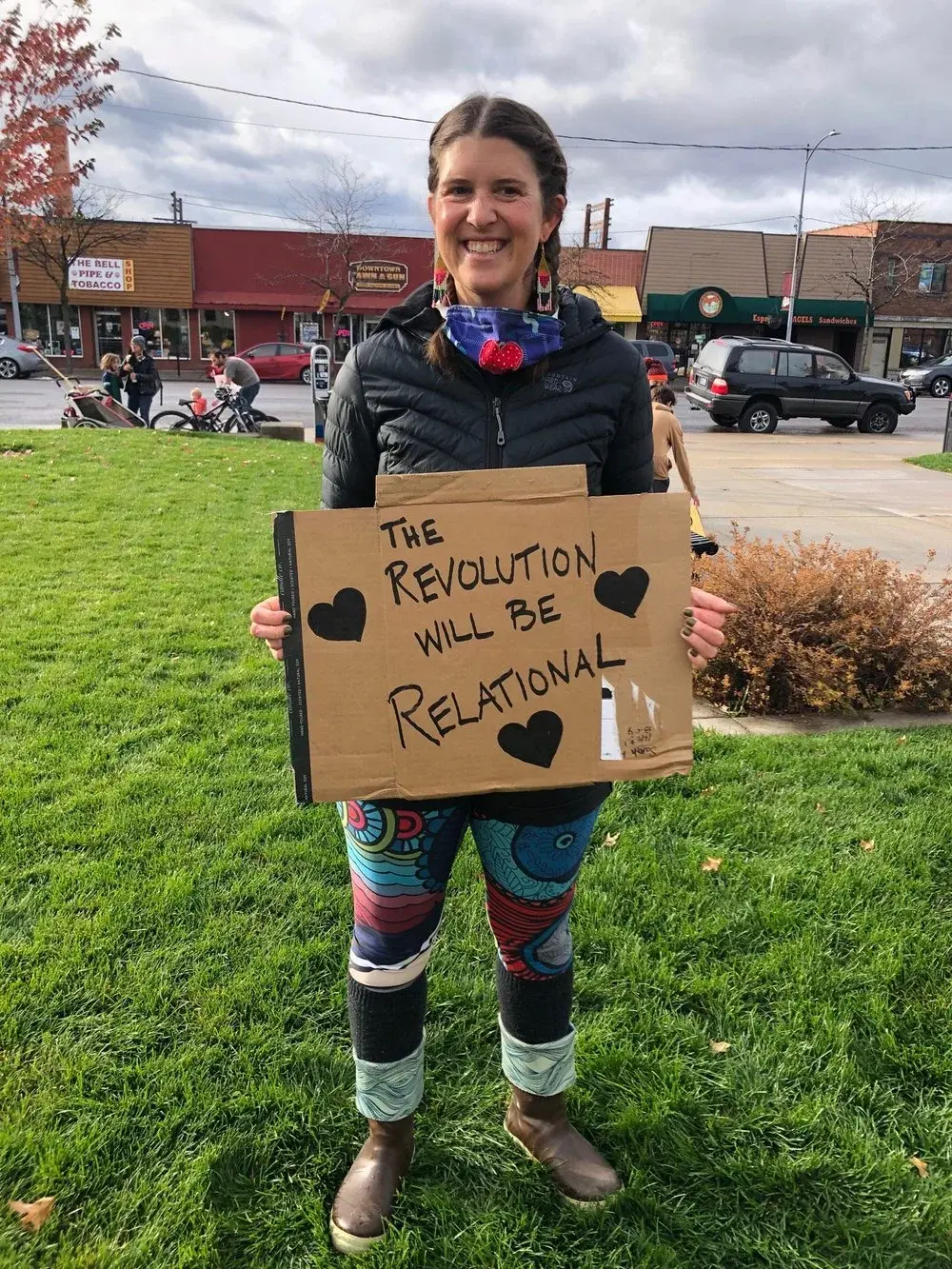 A woman smiles while holding a cardboard sign that reads "The Revolution will be relational."