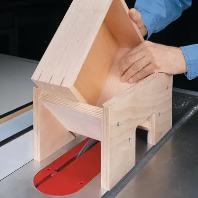 A person using a wooden jig on a table saw to cut a dovetail joint in a wooden box.