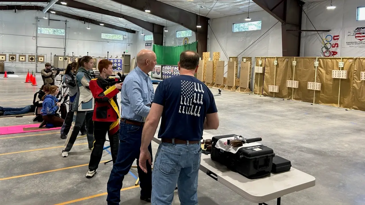 Young people practice shooting at an indoor range with instructors.
