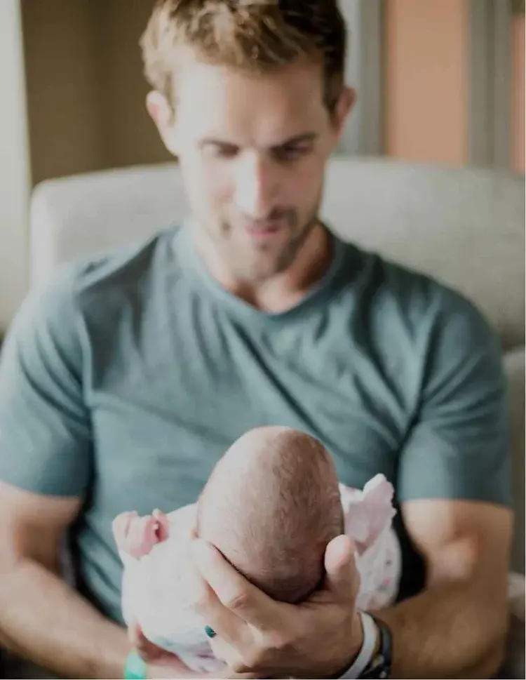 A man looks down at a newborn baby he is holding.