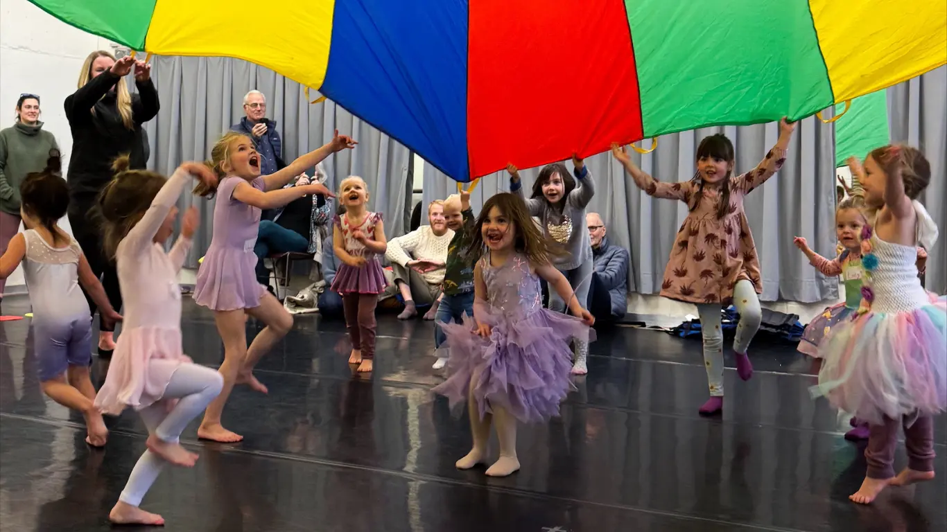 A group of children playing under a colored parachute.