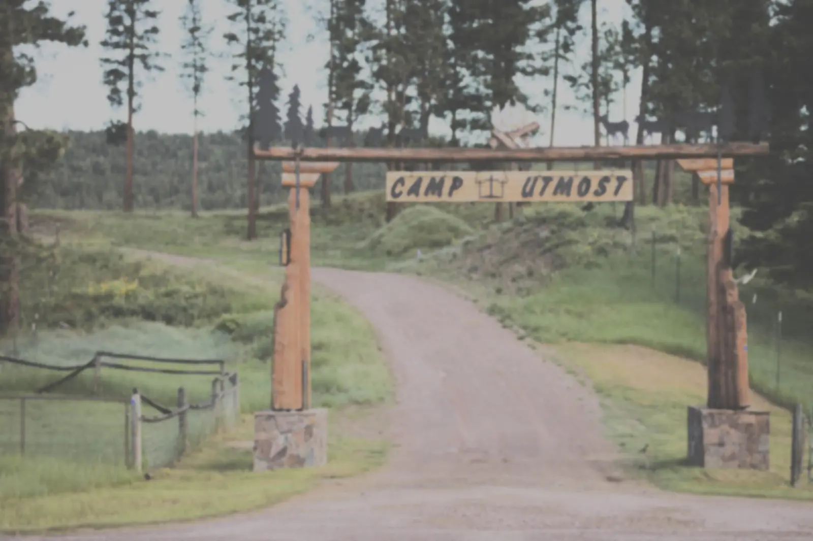 A rustic wooden archway spans a dirt road leading into a forested landscape.